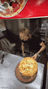 a man in a black shirt is cutting a pizza on a table