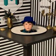 a boy in a blue hat is sticking his head out of a hole on a table