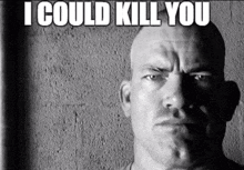 a man with a shaved head is standing in front of a wall with the words `` i could kill you '' .