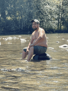 a man sits on a rock in the middle of a river