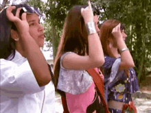 a group of young women are standing next to each other in a park and covering their eyes with their hands .