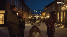 a group of people standing next to a reindeer on a snowy street with a netflix logo in the corner