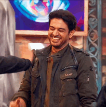 a man wearing an army jacket is laughing and shaking hands