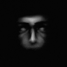 a black and white photo of a person 's face in the dark with glowing eyes .