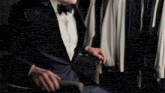 a man in a tuxedo sits in front of a rack of shirts