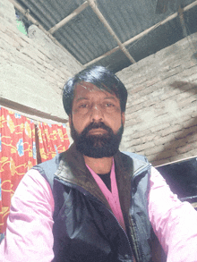 a man with a beard is wearing a pink shirt and black vest