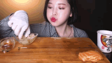 a woman is sitting at a table with a bowl of food and a cup that says ' ramen ' on it