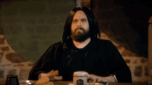 a man with long hair and a beard is sitting at a table with a cup of coffee