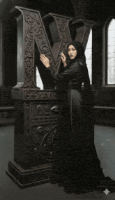 a woman in a black dress standing next to a large letter v
