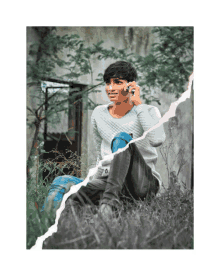 a young man is sitting in the grass talking on his cell phone