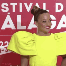 a woman in a bright yellow dress is standing in front of a red sign that says festival de malaga .