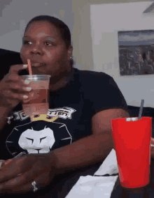 a woman is sitting at a table drinking a drink from a plastic cup with a straw .