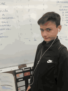 a boy wearing ear buds stands in front of a white board that says vietnam