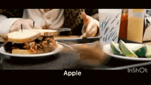 a person is sitting at a table eating a sandwich and a plate of apples