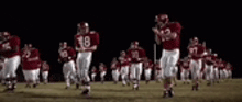 a group of football players in red uniforms are running on a field at night .