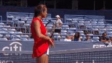 a woman in a red top is holding a tennis racquet on a tennis court with a citi sign in the background