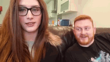 a man and a woman are sitting on a couch and looking at the camera .