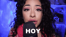 a woman with curly hair singing into a microphone with the word hoy above her