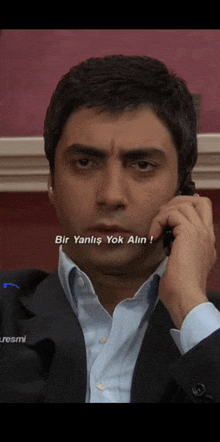 a man in a suit is talking on a cell phone with the words bir yanlis yok alin on the bottom