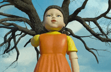 a doll is standing in front of a tree with a blue sky in the background