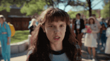 a girl with a serious look on her face is standing in front of a crowd of people