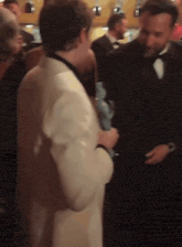 a man in a tuxedo is holding a trophy and talking to another man
