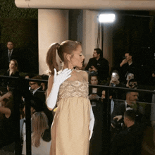 a woman in a dress and white gloves stands in front of a crowd of people
