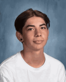 a young man wearing a white t-shirt and black earrings is posing for a portrait .