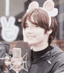 a young man wearing a headband with sheep ears holds a microphone and smiles