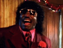 a man in a suit and tie is laughing with his mouth open and wearing sunglasses .
