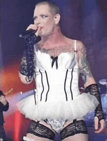 a man in a white corset and tutu is singing into a microphone on stage .