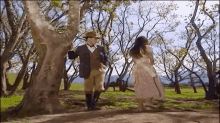 a man and a woman are standing next to a tree in the woods .