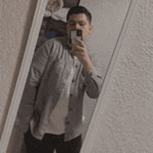 a man is taking a selfie in a mirror with his cell phone .