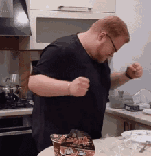 a man in a black shirt is standing in a kitchen with a bag of ramen in front of him