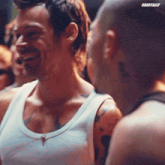 a man in a white tank top laughs while standing next to another man