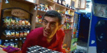 a man in a red shirt is standing in a store with a bunch of cans on the counter .