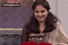 a woman is smiling and holding a red heart in her hands .