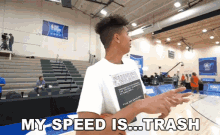 a man in a white shirt stands on a basketball court with the words " my speed is trash " above him