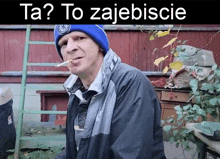 a man smoking a cigarette in front of a sign that says ta to zajebiscie