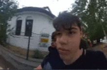 a young man is standing in front of a white house with a fence .