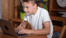 a young boy is sitting at a table using a laptop .