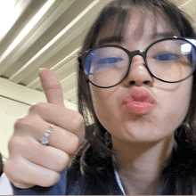 a woman wearing glasses and a ring on her finger gives a thumbs up