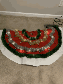 a red and white christmas tree skirt with green tinsel and lights