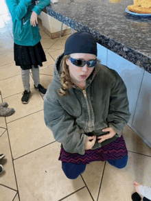 a girl wearing sunglasses and a beanie is kneeling down on the floor