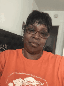 a woman wearing glasses and an orange shirt that says helen regina on it