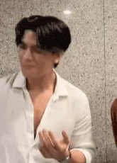 a man in a white shirt is standing in front of a wall and talking to someone .