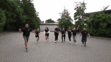 a group of people running on a brick pavement with a man wearing a black shirt with a green logo on the front