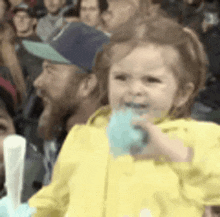 a little girl in a yellow jacket is eating cotton candy in a crowd .