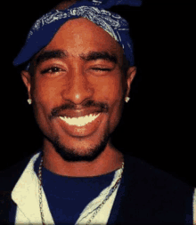 a close up of a man wearing a blue bandana and earrings smiling .