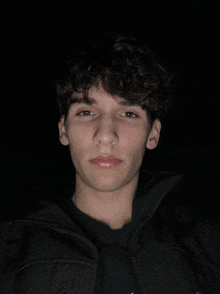 a young man with curly hair and a black jacket looks at the camera